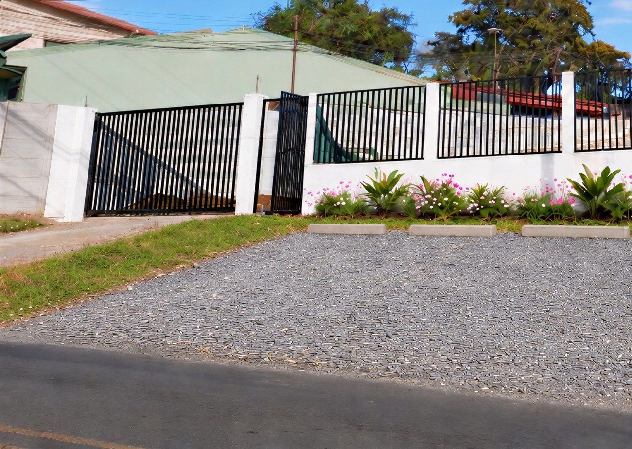 Entrada del residencial desde la calle, con tapia blanca, reja negra y portones para carros y peatones